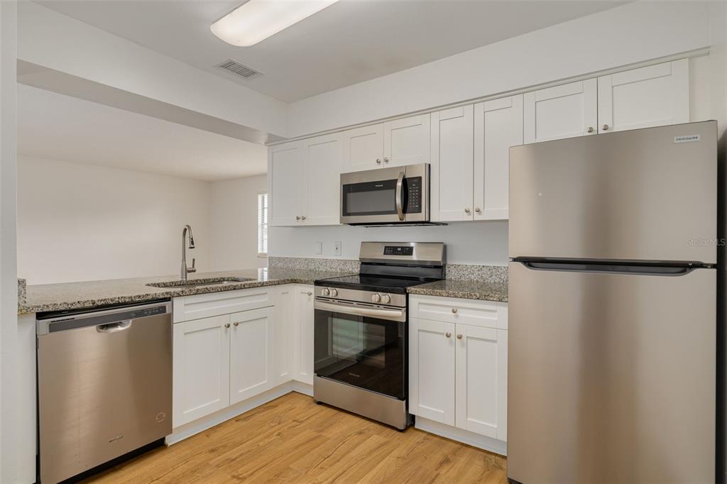 A kitchen features white cabinets, granite countertops, stainless steel appliances, and light wood flooring — 5715 S DALE MABRY HIGHWAY UNIT C, TAMPA, FL