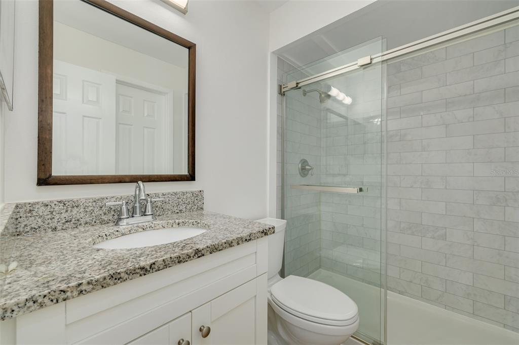 A bathroom features a granite vanity, white cabinet, framed mirror, and a glass-enclosed shower — 5715 S DALE MABRY HIGHWAY UNIT C, TAMPA, FL