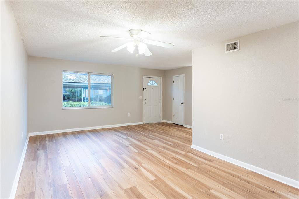 An empty living room features light wood-look flooring, a ceiling fan, and a front door — 501 SW 75TH STREET UNIT D13, GAINESVILLE, FL