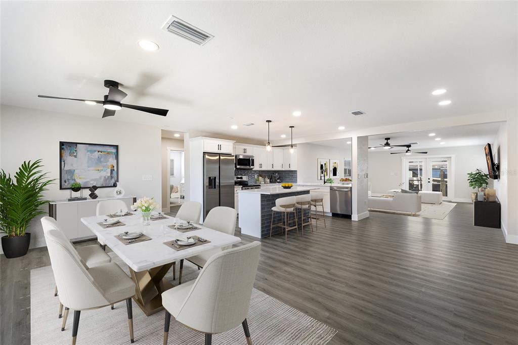An open-concept kitchen and dining area featuring a marble-topped table, island seating, and wood flooring — 10316 KINGFISHER ROAD W, BRADENTON, FL