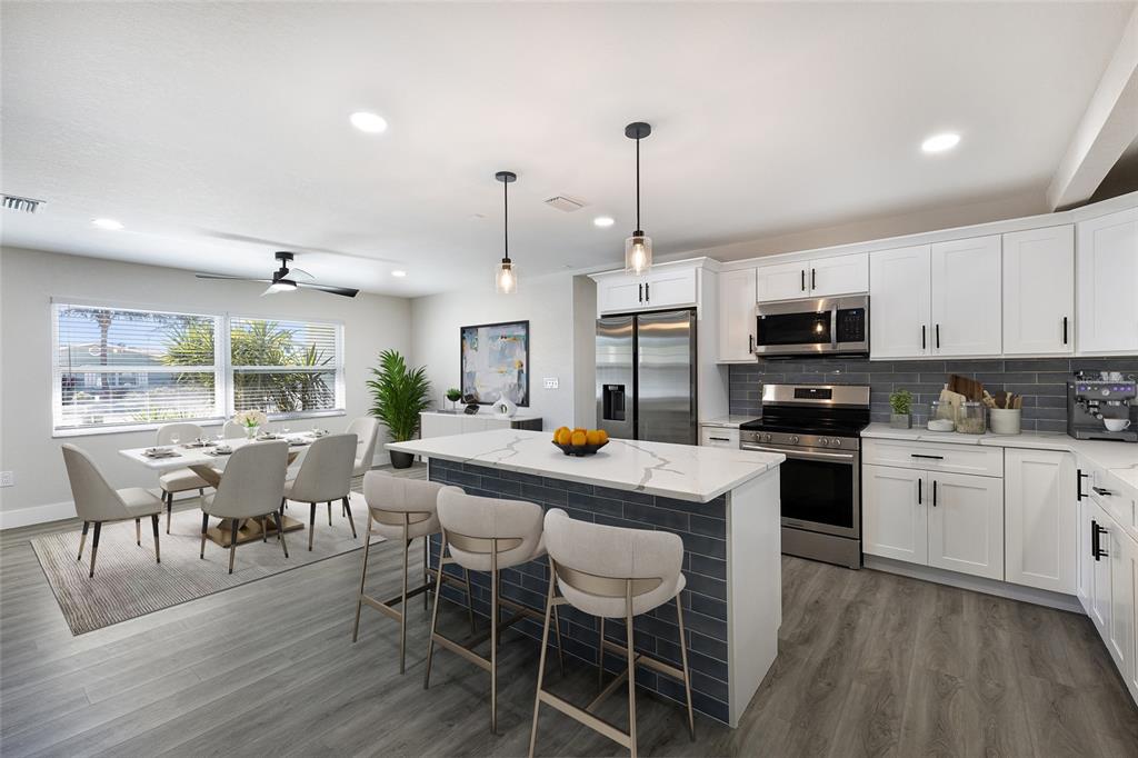 A modern kitchen features white cabinets, a marble-topped island, and an adjacent dining area — 10316 KINGFISHER ROAD W, BRADENTON, FL