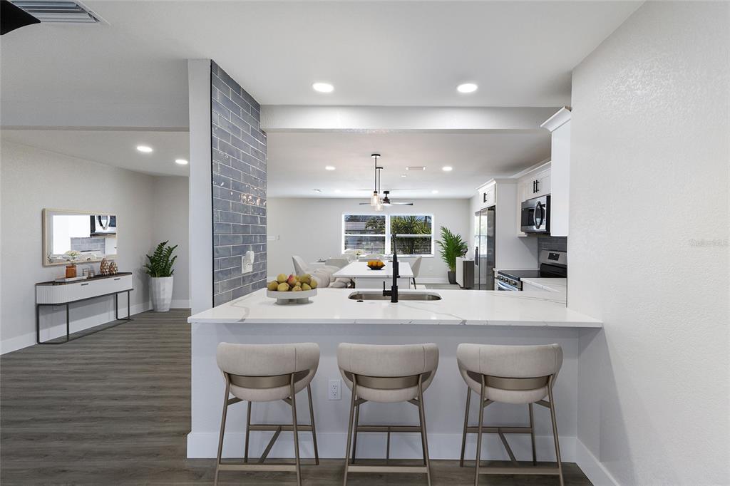 A kitchen features a white quartz island with three bar stools and a blue-tiled accent wall — 10316 KINGFISHER ROAD W, BRADENTON, FL