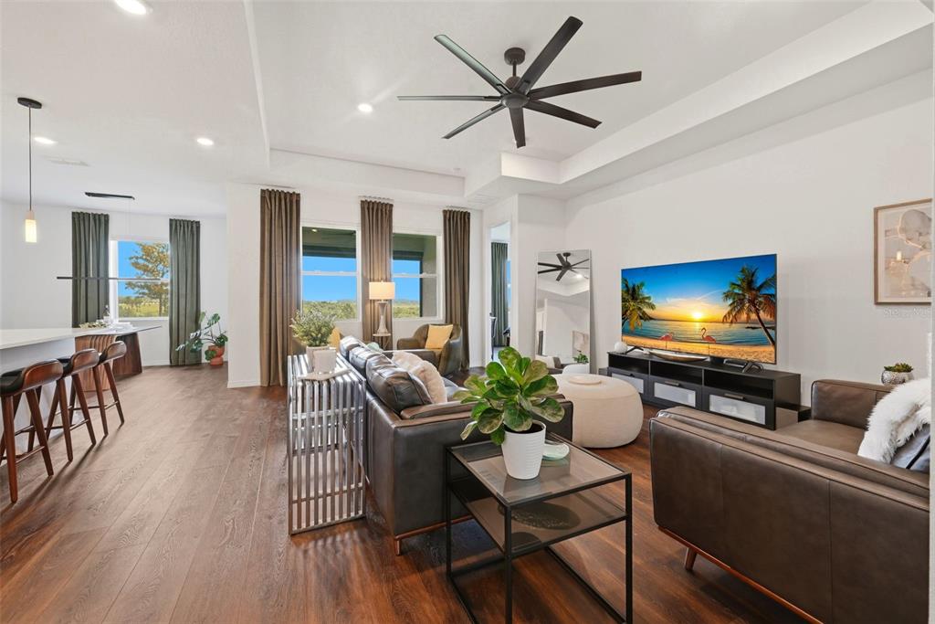 A modern living room features dark wood floors, leather furniture, and a large television — 2346 GOLD DUST DRIVE, MINNEOLA, FL