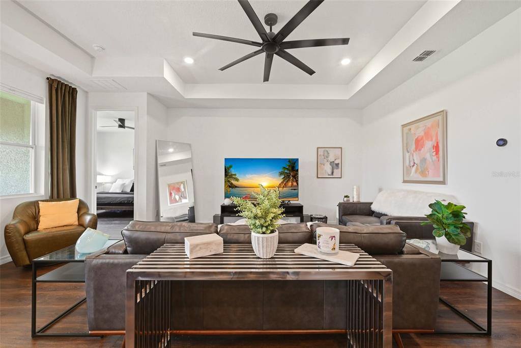 A living room features a tray ceiling, a large ceiling fan, and dark leather furniture — 2346 GOLD DUST DRIVE, MINNEOLA, FL