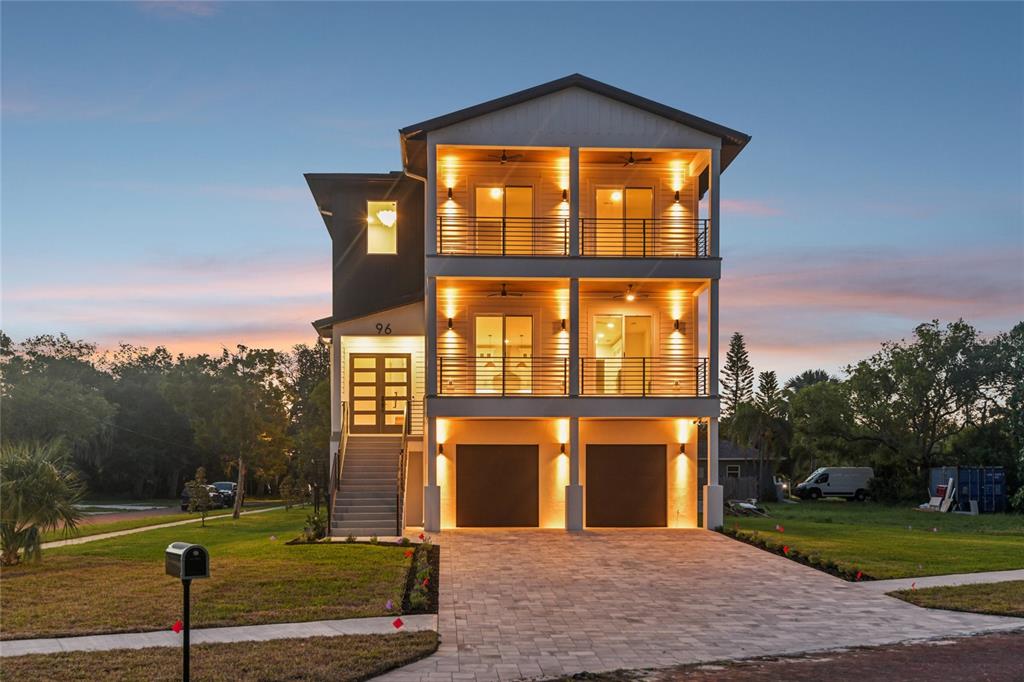 A three-story house with two garage doors, two levels of balconies, and exterior lighting — 96 SHORE DRIVE, TARPON SPRINGS, FL