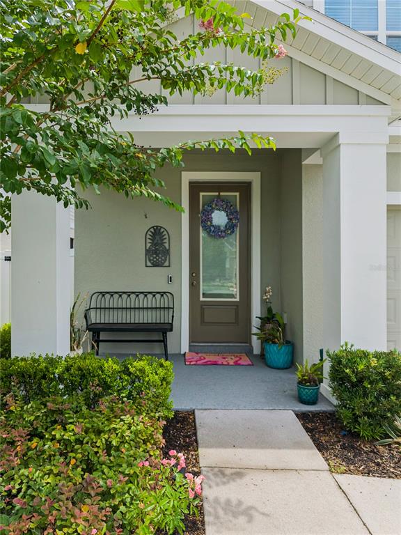 A covered front porch features a black bench, a brown door with a wreath, and landscaping — 4222 HIBISCUS BLOOM DRIVE, ORLANDO, FL