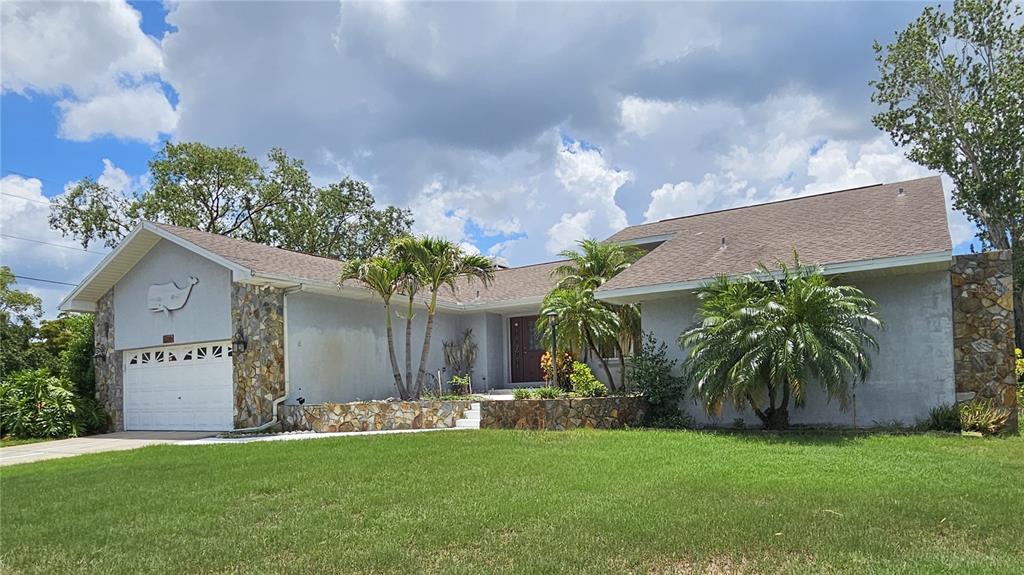 A single-story house with a stone facade, a garage, and palm trees in the yard — 2210 BAYOU DRIVE, HOLIDAY, FL