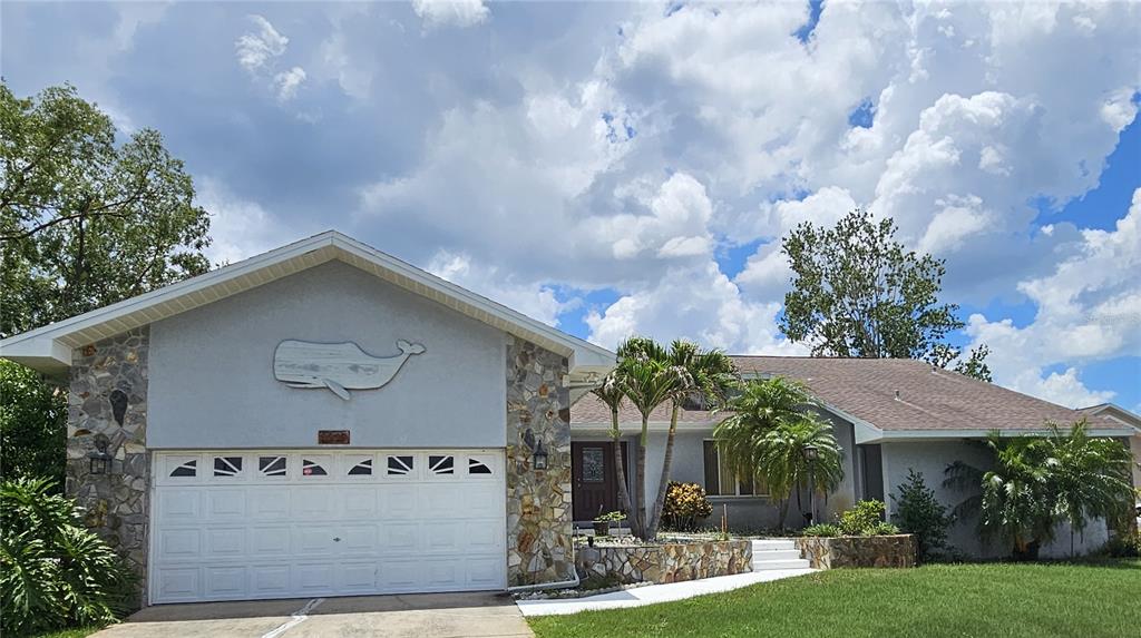 A single-story house features a stone-accented facade, a two-car garage, and a whale wall decoration — 2210 BAYOU DRIVE, HOLIDAY, FL