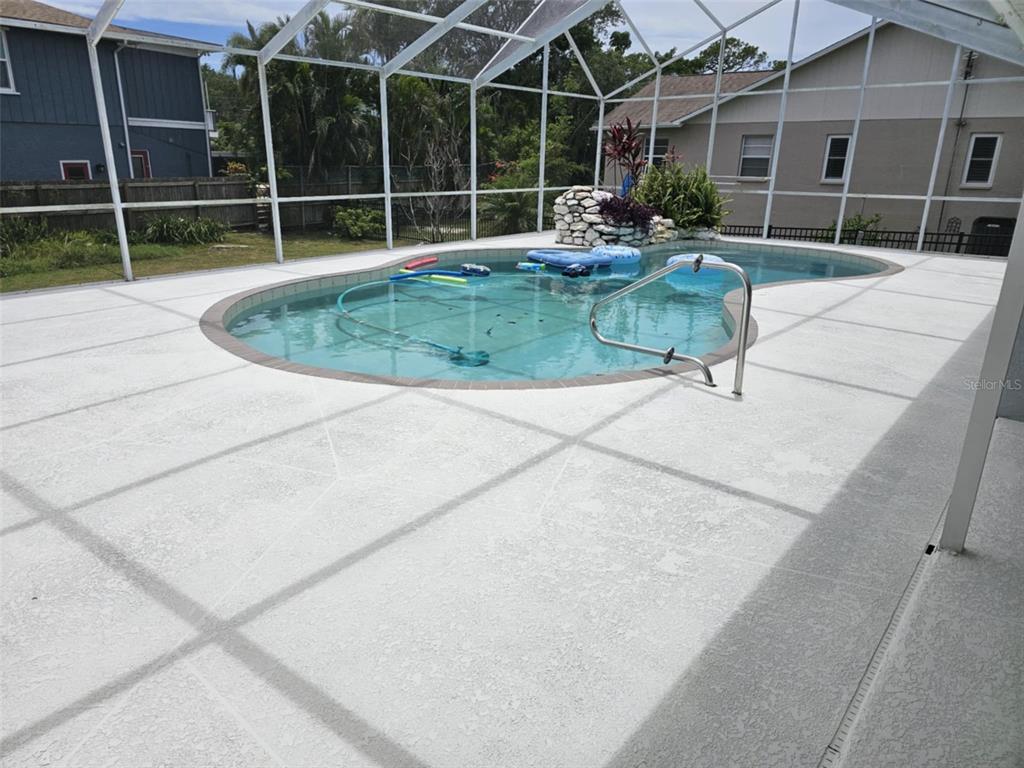 A screened-in swimming pool with a rock water feature sits on a concrete patio — 2210 BAYOU DRIVE, HOLIDAY, FL
