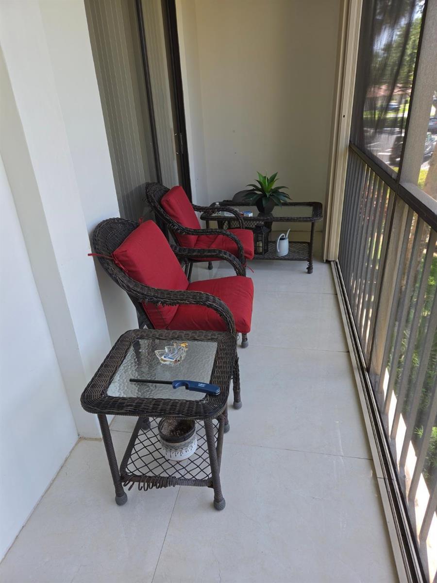A screened-in balcony features two wicker chairs with red cushions and two glass-topped tables — 5310 Las Verdes Circle # 220, Delray Beach FL 33484, DELRAY BEACH, FL