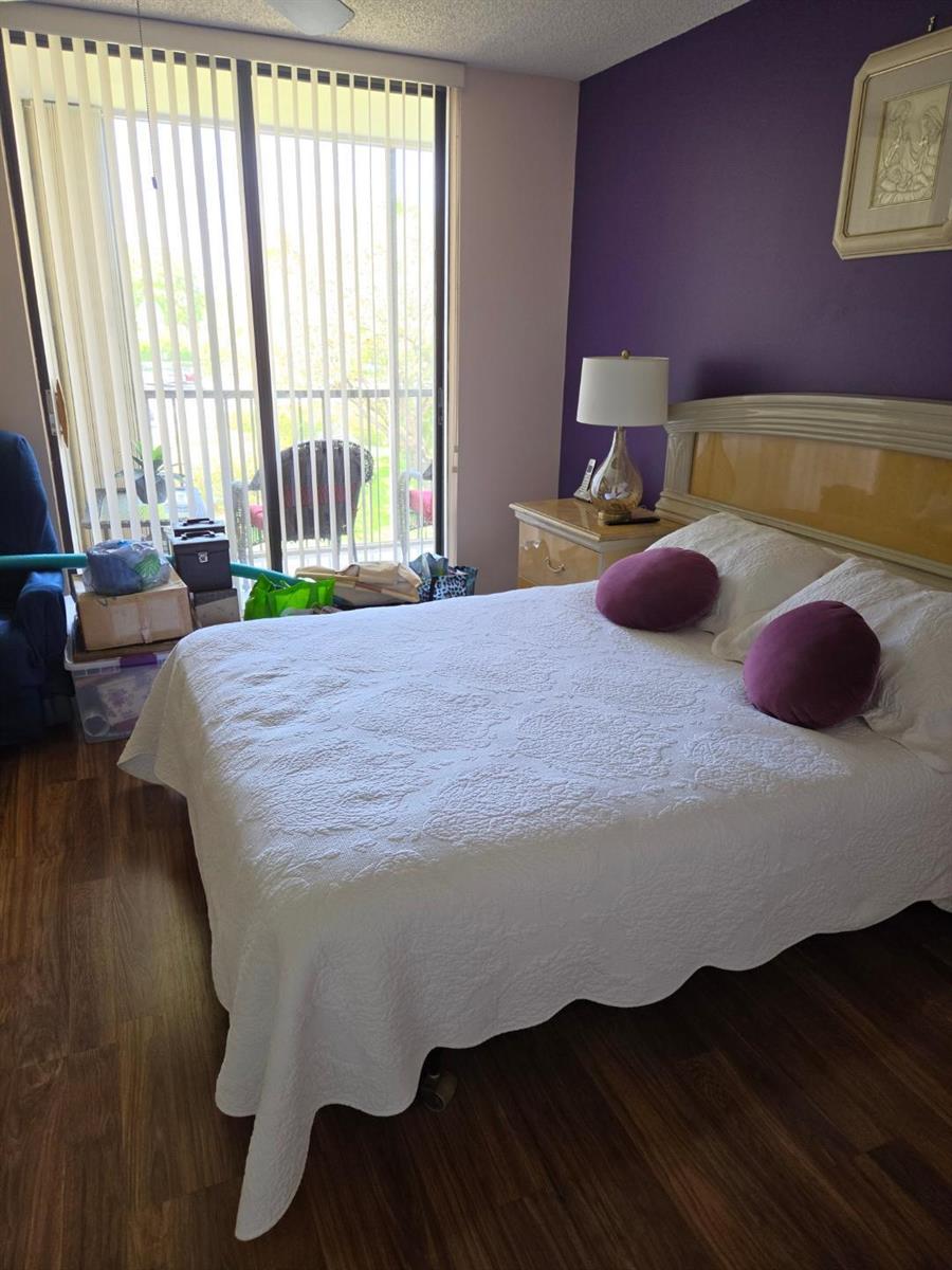 A bedroom with a white bed, purple accent wall, and a sliding glass door — 5310 Las Verdes Circle # 220, Delray Beach FL 33484, DELRAY BEACH, FL