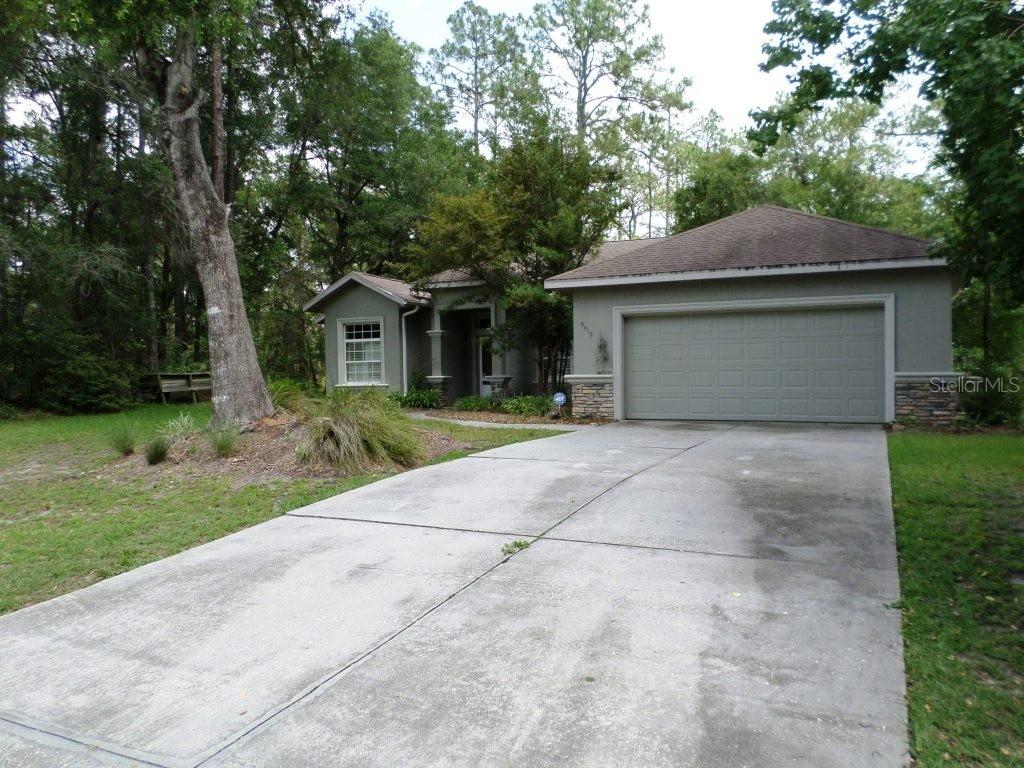 A single-story house with a concrete driveway, a two-car garage, and surrounding trees — 9419 N COUNTRY CLUB WAY, DUNNELLON, FL
