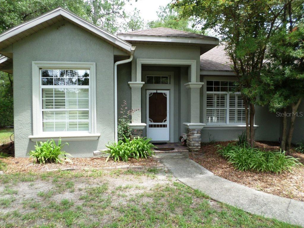 The exterior of a single-story house features a light green stucco facade and stone columns — 9419 N COUNTRY CLUB WAY, DUNNELLON, FL