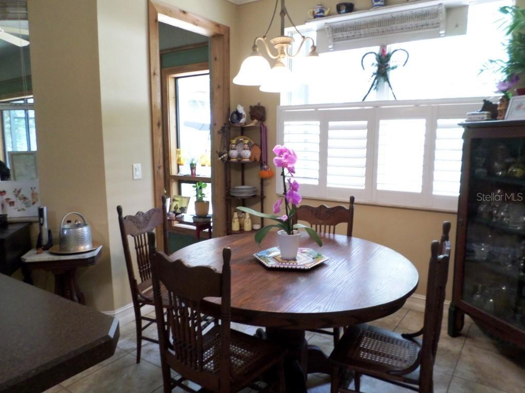 A dining room features a round wooden table, four chairs, and a window with shutters — 9419 N COUNTRY CLUB WAY, DUNNELLON, FL