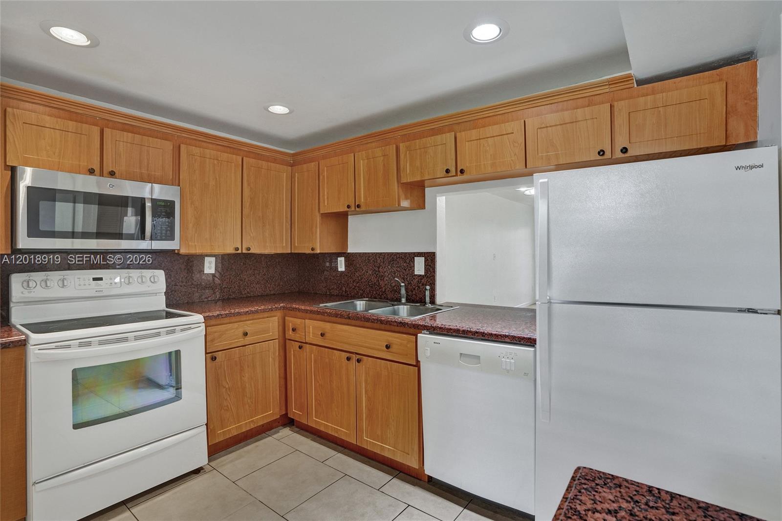 A kitchen features wood cabinets, granite countertops, white appliances, and light-colored tile flooring — 1601 NE 191 ST # B112, Miami FL 33179, MIAMI, FL
