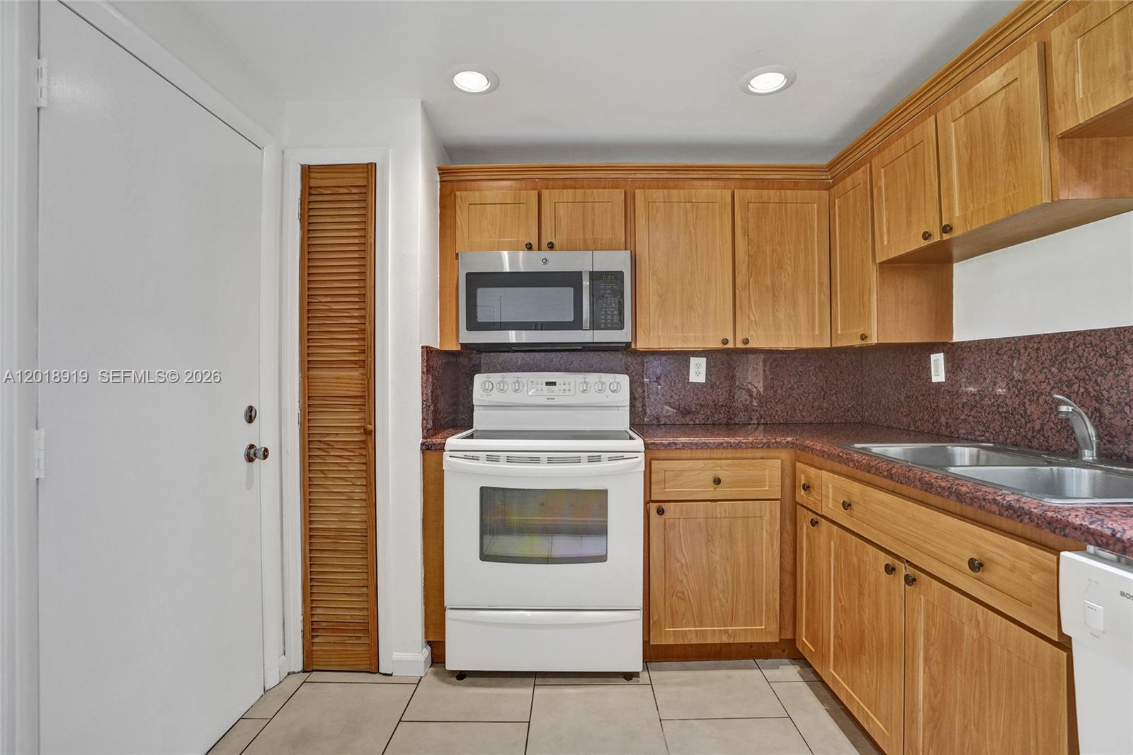 A kitchen features wood cabinets, a white stove, a microwave, and red granite countertops — 1601 NE 191 ST # B112, Miami FL 33179, MIAMI, FL