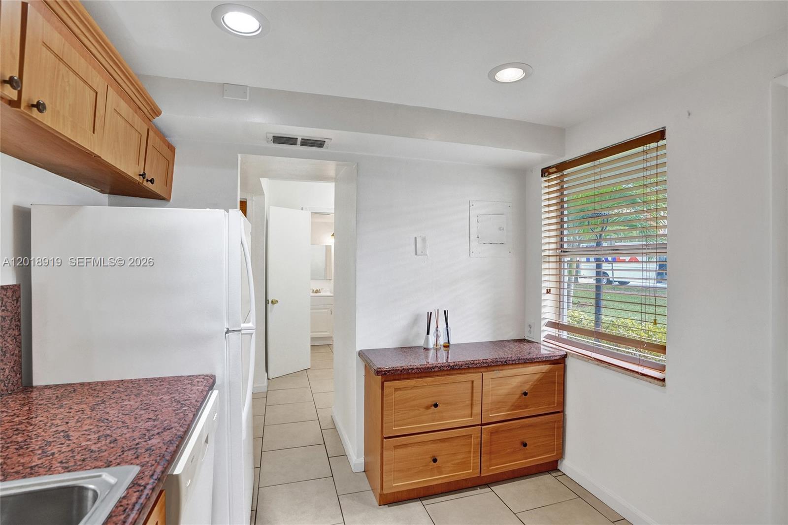 A kitchen features wood cabinets, granite countertops, a white refrigerator, and a window with blinds — 1601 NE 191 ST # B112, Miami FL 33179, MIAMI, FL