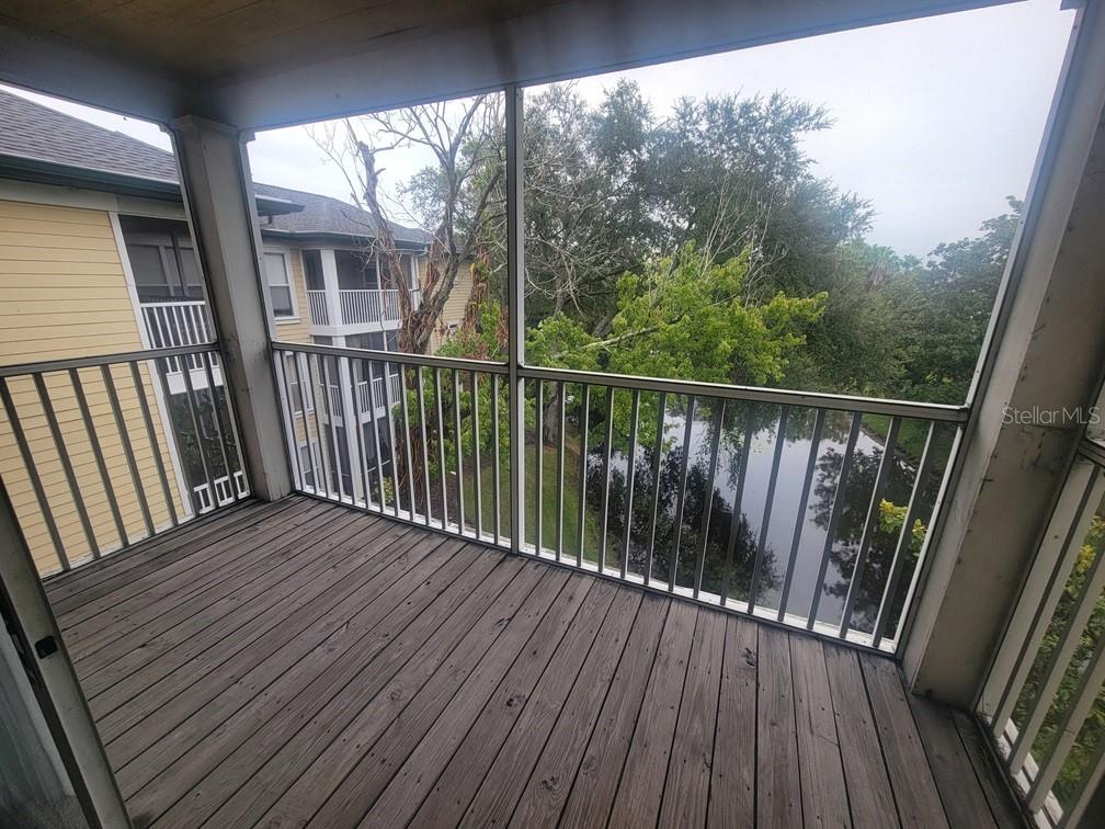 A screened-in balcony with wood flooring overlooks a pond and neighboring apartment buildings — 10020 STRAFFORD OAK COURT UNIT 923, TAMPA, FL