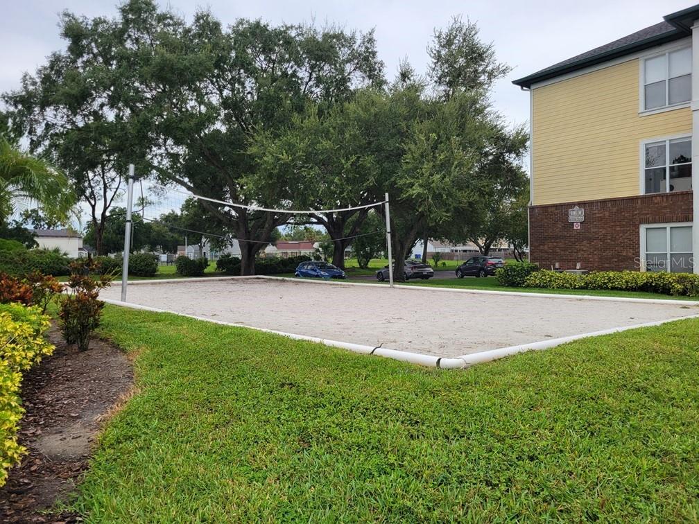 A sand volleyball court sits in front of a multi-story apartment building with yellow siding — 10020 STRAFFORD OAK COURT UNIT 923, TAMPA, FL