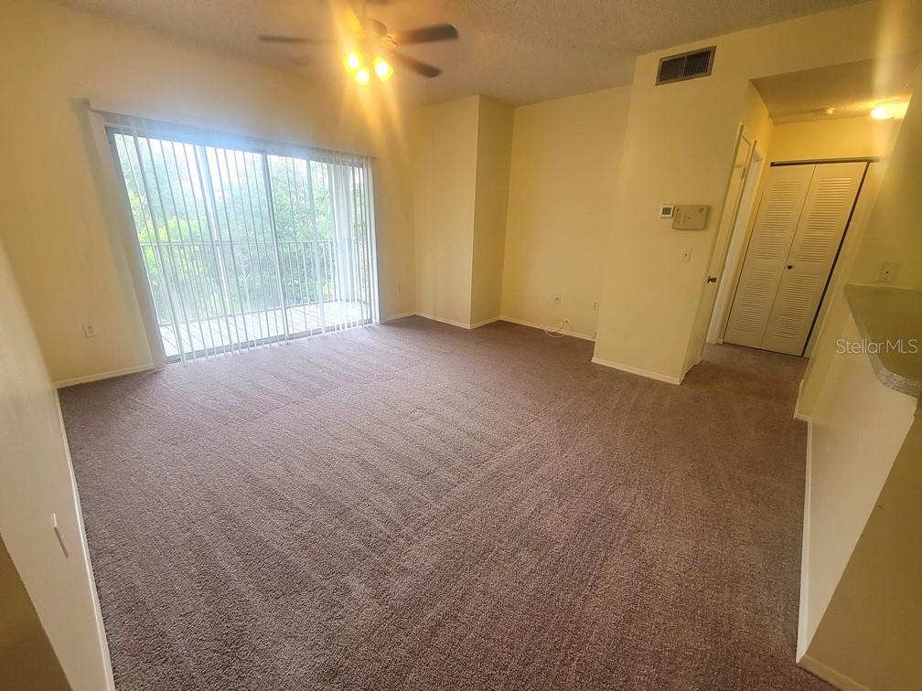 An empty living room features beige carpet, light yellow walls, and a sliding glass door — 10020 STRAFFORD OAK COURT UNIT 923, TAMPA, FL