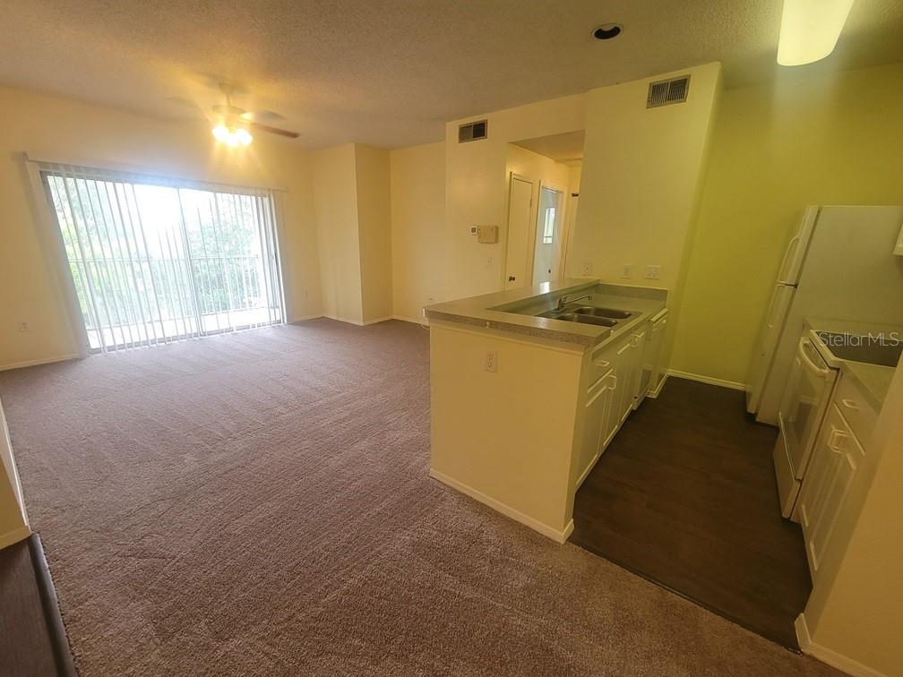 An open-concept living area features carpeted flooring, a kitchen island, and sliding glass balcony doors — 10020 STRAFFORD OAK COURT UNIT 923, TAMPA, FL
