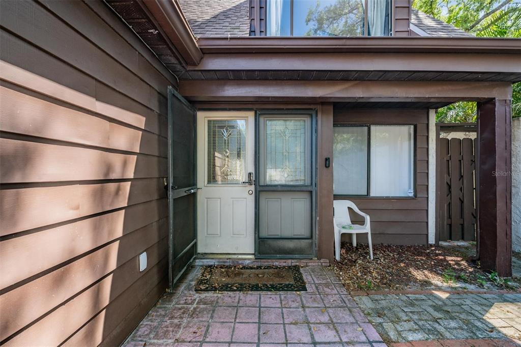 A brown-sided house exterior features a front door with a screen and a patio — 7300 BELLOWS FALLS LANE, HUDSON, FL