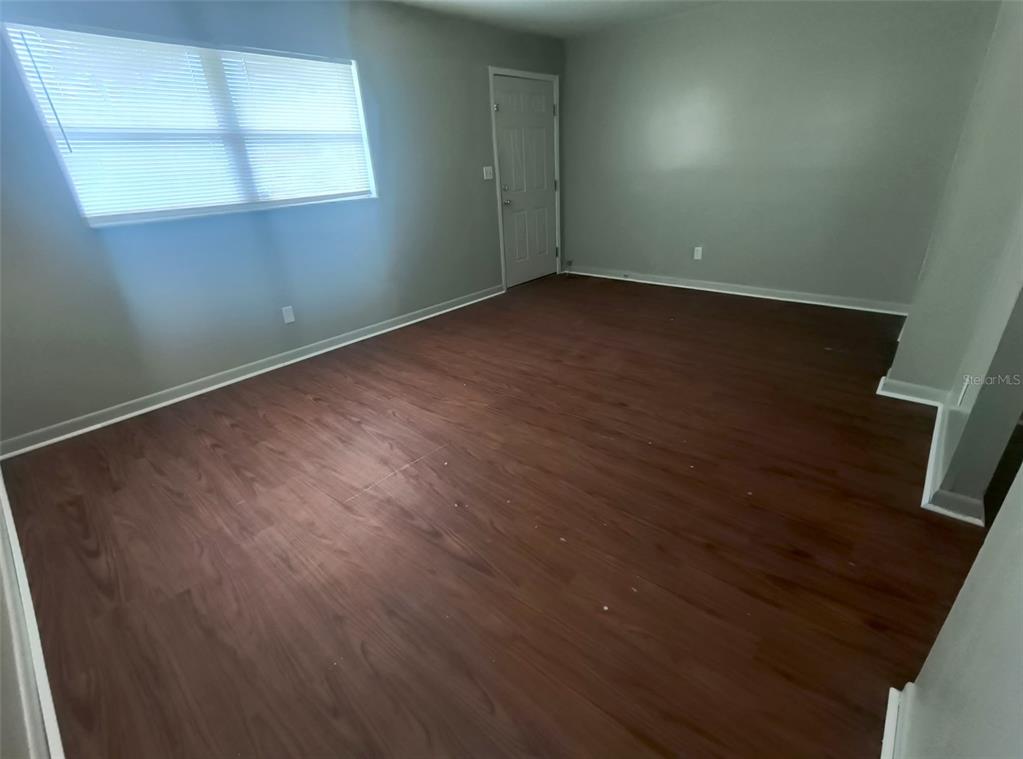 An empty room features wood-look flooring, light gray walls, and a single window with blinds — 401 HIBISCUS AVENUE UNIT 13, BUNNELL, FL