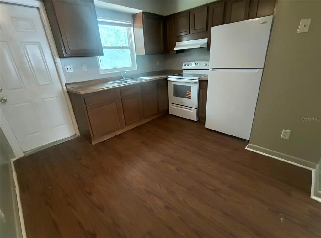 A kitchen features dark wood cabinets, a white stove, a white refrigerator, and wood-look flooring — 401 HIBISCUS AVENUE UNIT 13, BUNNELL, FL