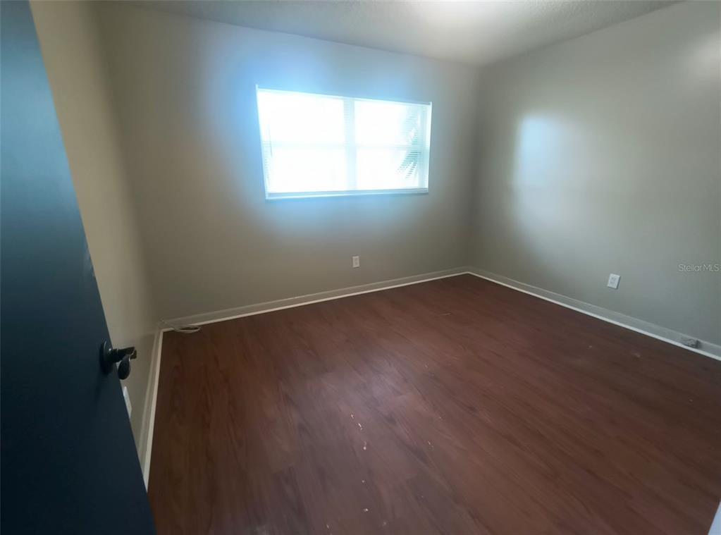 An empty bedroom features light gray walls, dark wood-look flooring, and a single window — 401 HIBISCUS AVENUE UNIT 13, BUNNELL, FL