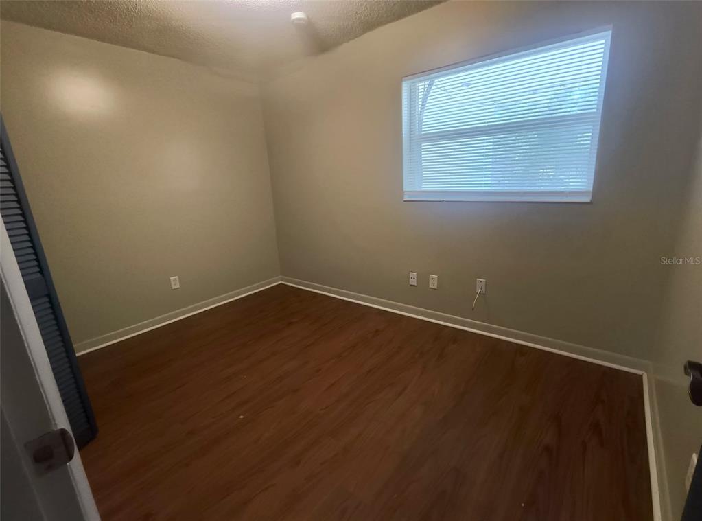 An empty bedroom features light gray walls, dark wood-look flooring, and a window with blinds — 401 HIBISCUS AVENUE UNIT 13, BUNNELL, FL