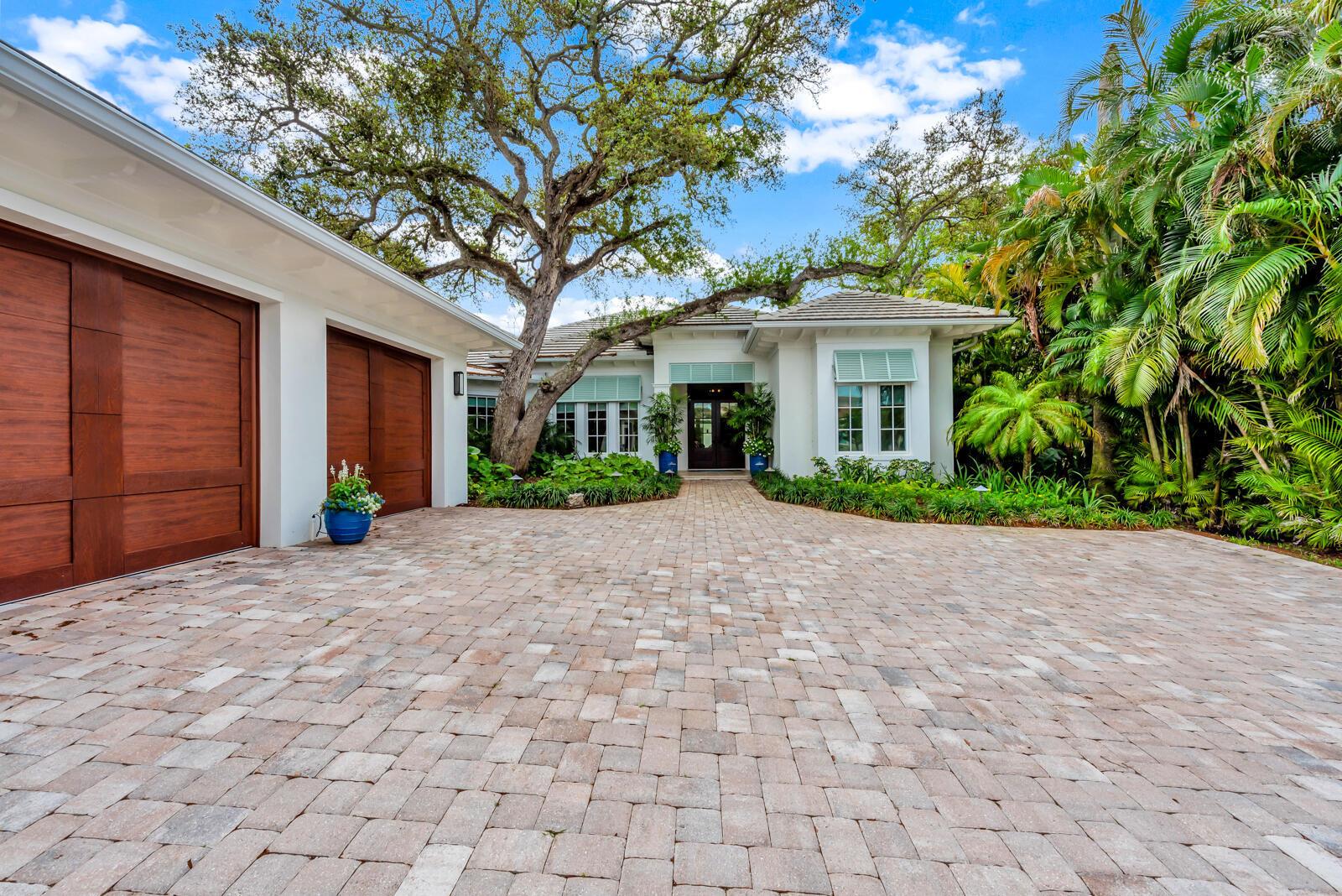 A paved driveway leads to the entrance of a white house with wooden garage doors — 544 Live Oak Road, Vero Beach FL 32963, VERO BEACH, FL