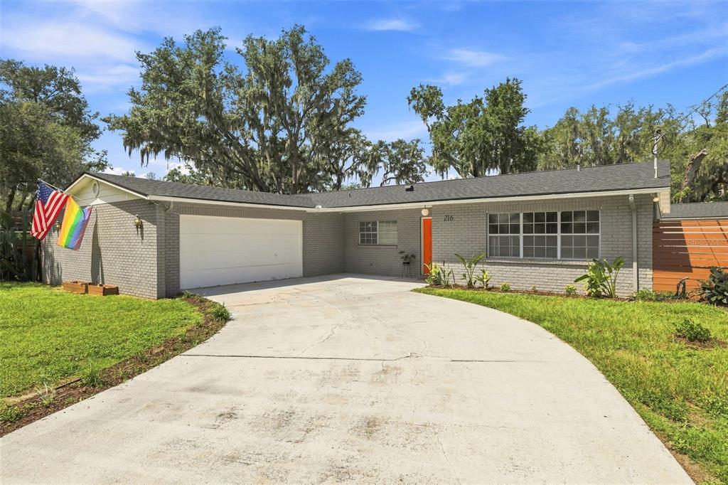 A single-story gray brick house with a concrete driveway, a white garage, and two flags — 216 AMANA AVENUE, BRANDON, FL