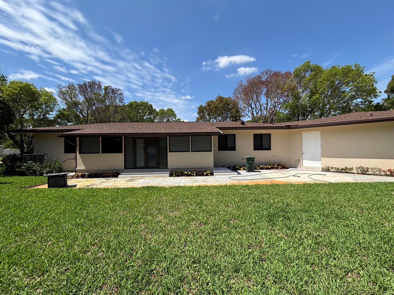 A single-story house with a beige exterior, brown roof, and a large stone patio — 135 E Ilex Drive, Lake Park FL 33403, LAKE PARK, FL