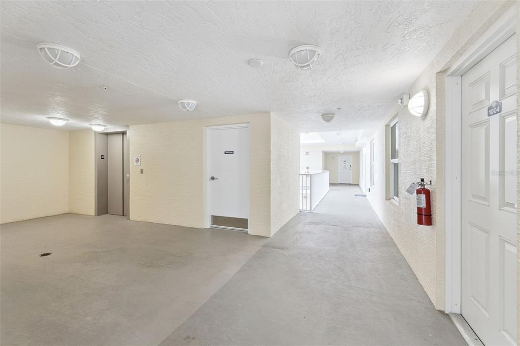 A bright, covered outdoor apartment hallway features a gray floor, white walls, and an elevator — 3721 S ATLANTIC AVENUE UNIT 1004, DAYTONA BEACH, FL