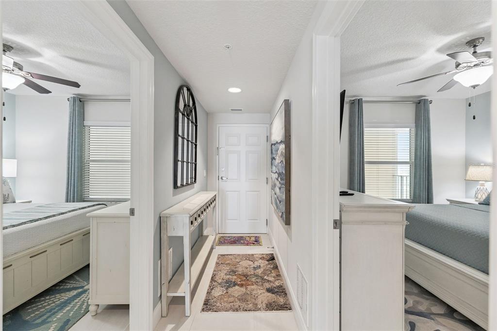 A hallway with a white door, console table, and two bedrooms on either side — 3721 S ATLANTIC AVENUE UNIT 1004, DAYTONA BEACH, FL