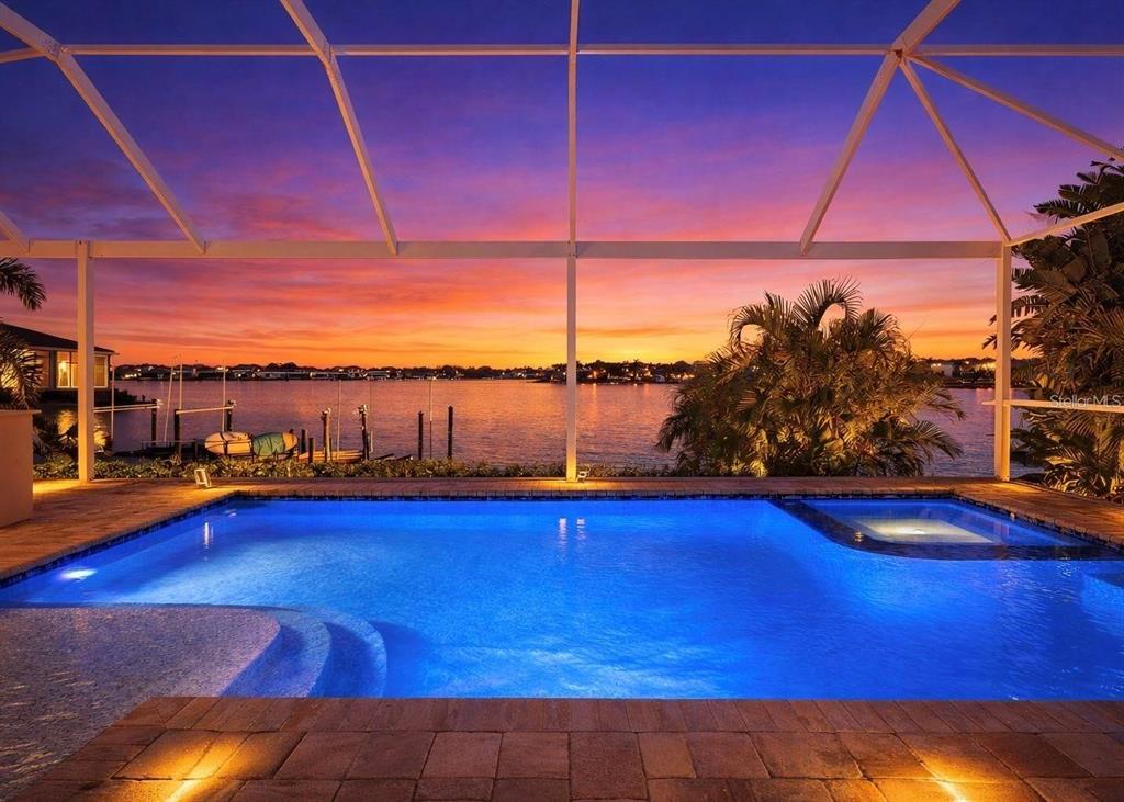 A swimming pool with a spa sits inside a screened enclosure overlooking a sunset waterfront — 5237 BRIGHTON SHORE DRIVE, APOLLO BEACH, FL