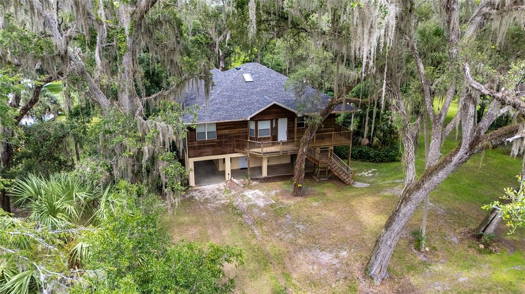 An elevated wooden house with a shingled roof sits among trees draped in Spanish moss — 2299 N BAYOU POINT, INVERNESS, FL