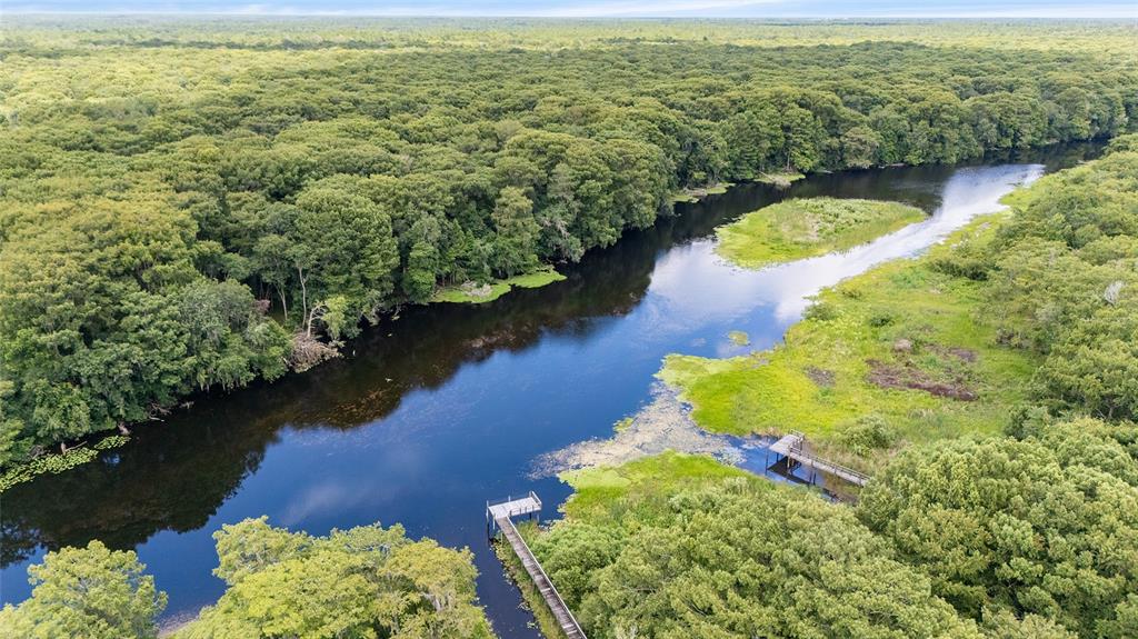 An aerial view shows a river flowing through a dense forest with two wooden docks — 2299 N BAYOU POINT, INVERNESS, FL