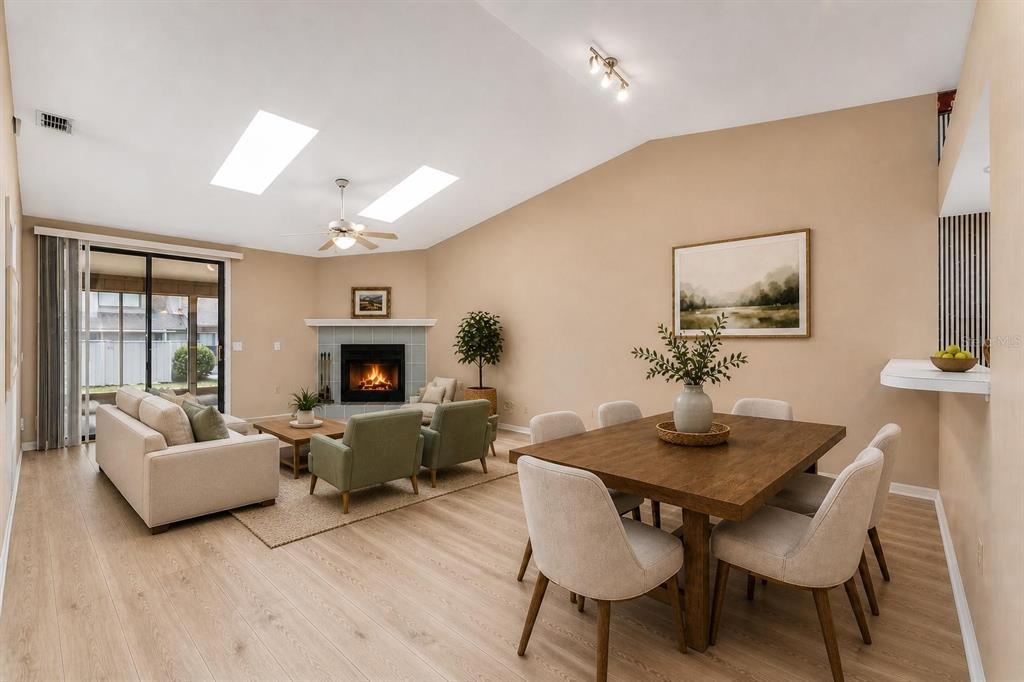 A living and dining area with light wood floors, a fireplace, and vaulted ceilings — 3725 NW 58TH PLACE, GAINESVILLE, FL