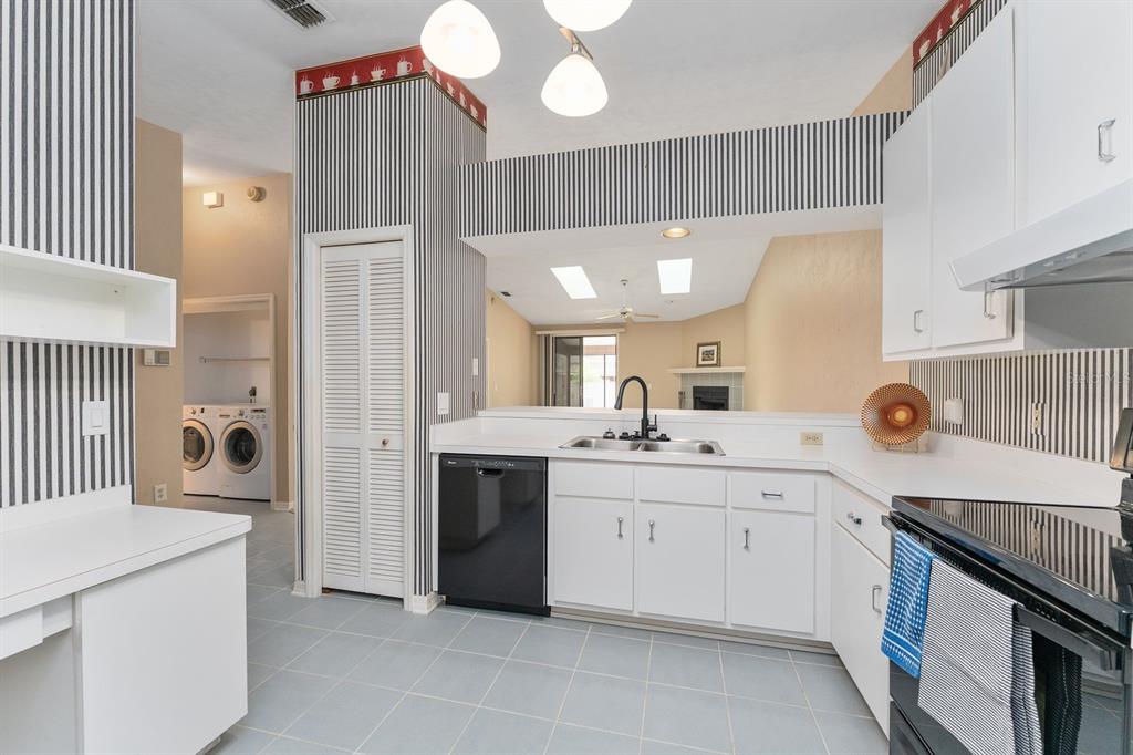A kitchen with white cabinets, black appliances, striped wallpaper, and a view into the living area — 3725 NW 58TH PLACE, GAINESVILLE, FL