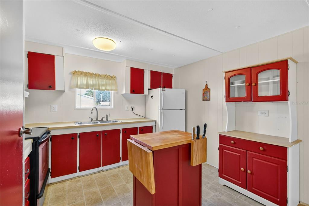 A kitchen features red cabinets, a white refrigerator, a wooden island, and light-colored flooring — 563 TAMMI DRIVE, LEESBURG, FL