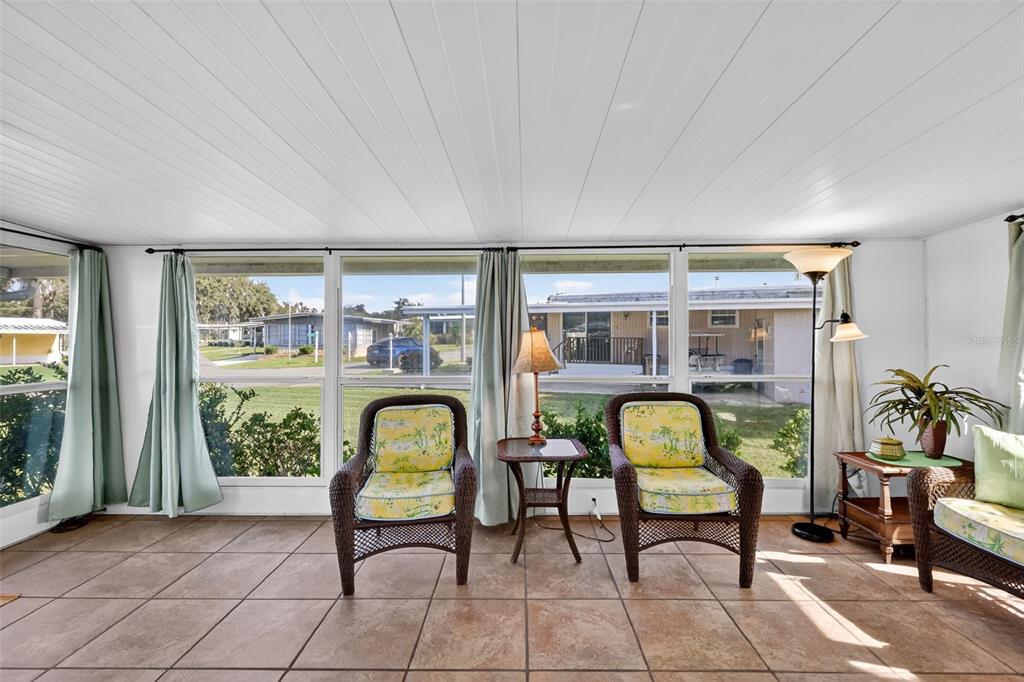 A sunroom features tiled floors, wicker chairs with yellow cushions, and large windows overlooking outdoors — 563 TAMMI DRIVE, LEESBURG, FL