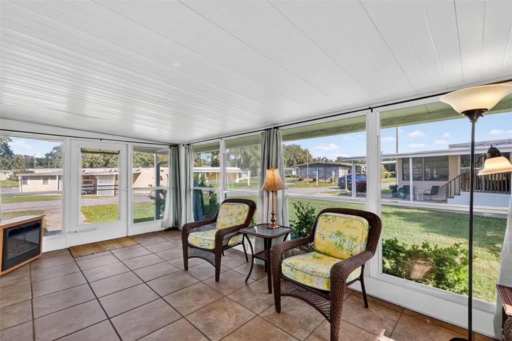 A sunroom features tile flooring, wicker chairs, and large windows overlooking a residential neighborhood — 563 TAMMI DRIVE, LEESBURG, FL