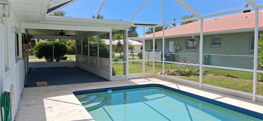 A swimming pool sits inside a screened-in lanai next to a covered patio area — 441 RUBENS DRIVE E, NOKOMIS, FL