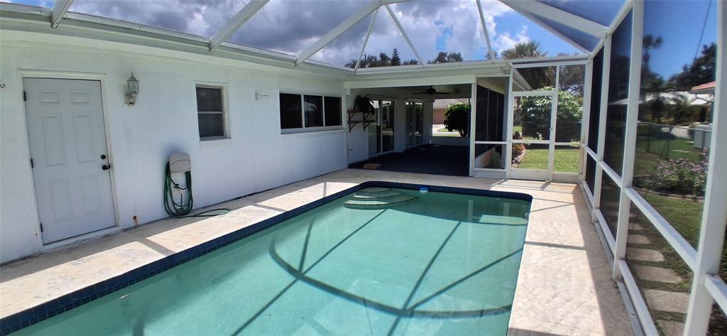A swimming pool sits inside a screened-in lanai attached to a white house — 441 RUBENS DRIVE E, NOKOMIS, FL