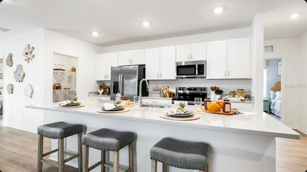A modern kitchen features white cabinets, stainless steel appliances, and a large quartz island — 5455 ISLA SAONA DRIVE, KISSIMMEE, FL
