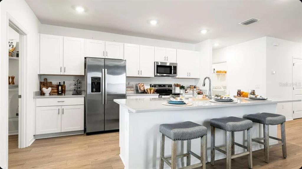 A modern kitchen features white cabinets, stainless steel appliances, a large island, and wood flooring — 5455 ISLA SAONA DRIVE, KISSIMMEE, FL