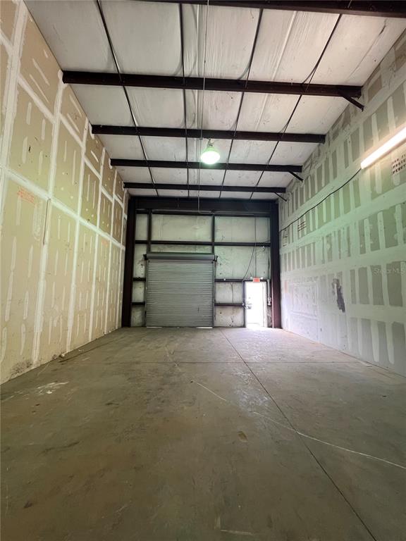 An empty warehouse space features unfinished drywall walls, a concrete floor, and a roll-up door — 7216 CHANCERY UNIT 200, ORLANDO, FL