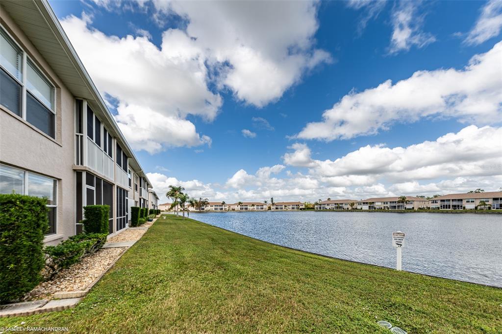 A multi-story apartment building sits beside a large lake under a blue, cloudy sky — 11644 SW EGRET CIRCLE UNIT 908, LAKE SUZY, FL