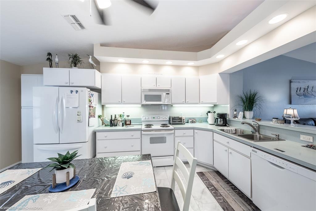 A kitchen features white cabinetry, white appliances, a breakfast table, and recessed lighting — 11644 SW EGRET CIRCLE UNIT 908, LAKE SUZY, FL